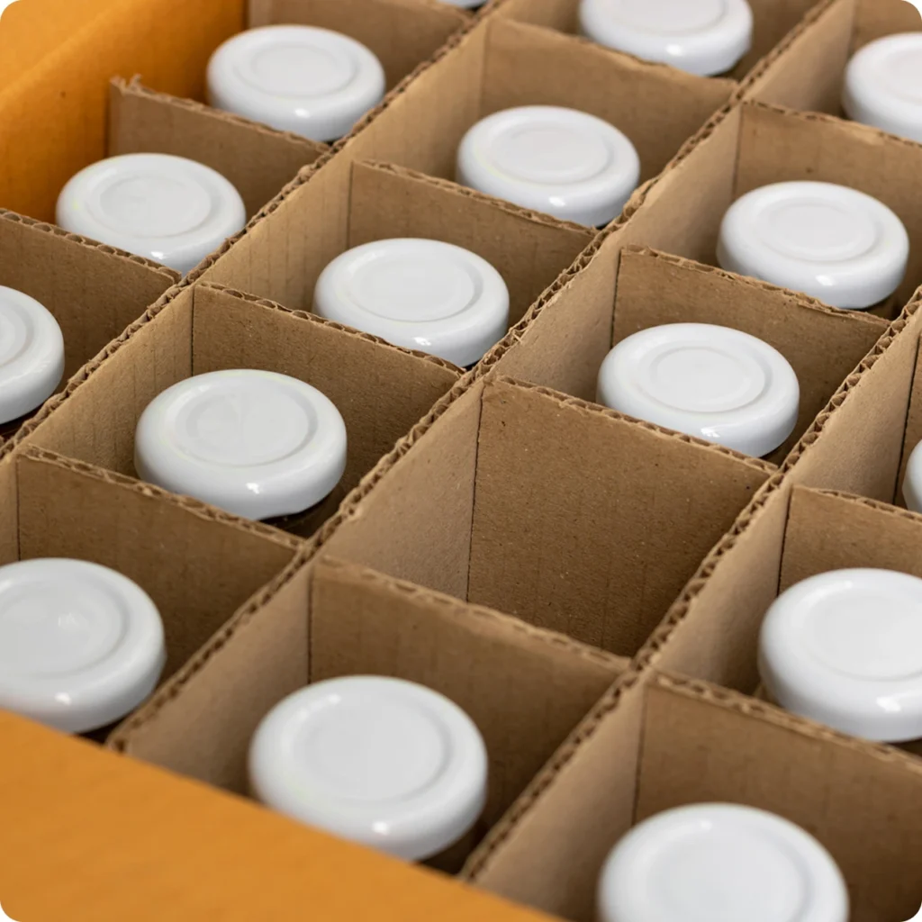 A cardboard box with multiple compartments, each holding a small white jar or bottle with a white lid, viewed from above.