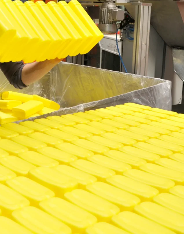 A person handles bright yellow rectangular plastic containers, arranging them in an organized manner on a table in an industrial setting.